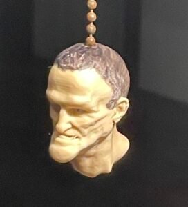 A #6 ball chain, as for an electric light, from which hangs a little head of an ugly dude